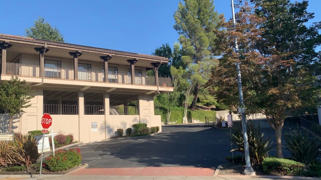 Exterior view of the Orinda acupuncture clinic building, featuring a stop sign and surrounding greenery under a clear blue sky.
